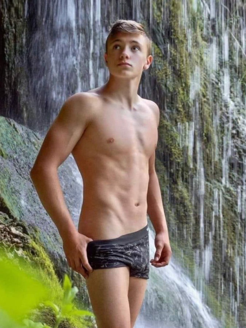 Boy poses at a waterfall adjusting his swimming trunks.